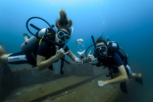 Two scuba divers exploring underwater, holding a plastic bottle, symbolizing ocean clean-up efforts.