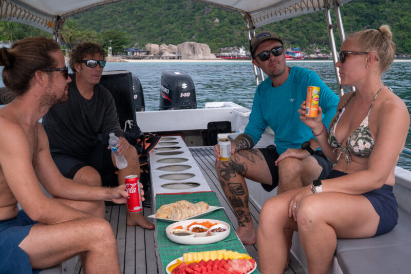 Friends enjoying drinks and snacks on a boat trip near a scenic coastline.