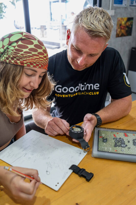 Two people study a map and compass at a table, learning navigation skills indoors.