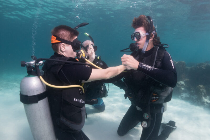 two men in scuba gear holding hands underwater