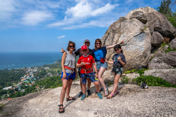 Family hiking on a rock overlooking the ocean and a coastal town with clear blue skies.