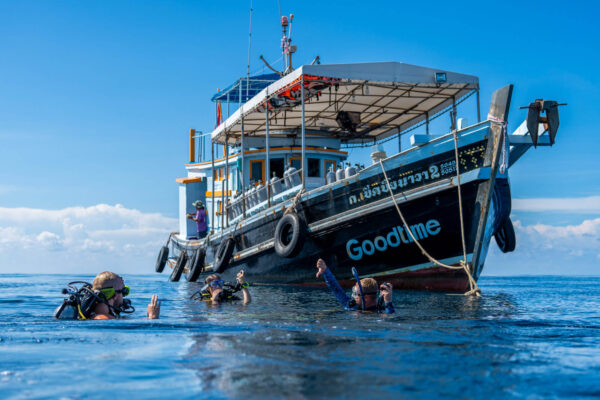 Divers explore ocean near a dive boat named Goodtime under a clear blue sky.