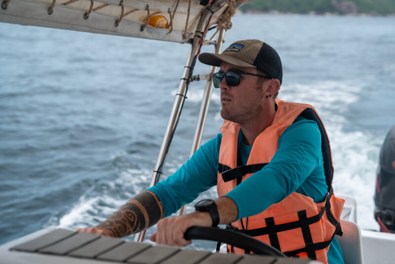Man wearing life jacket and cap, steering a boat on the ocean with focus and determination.