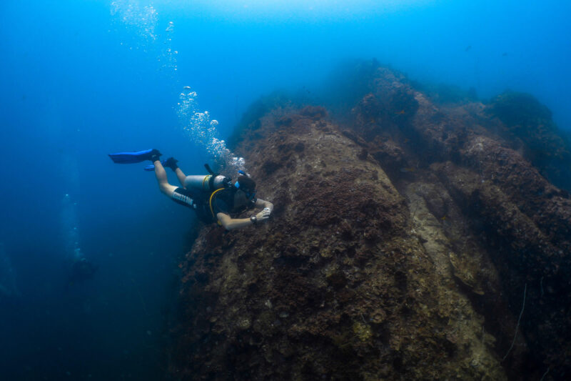 Scuba diver exploring a rocky underwater terrain in deep blue ocean.