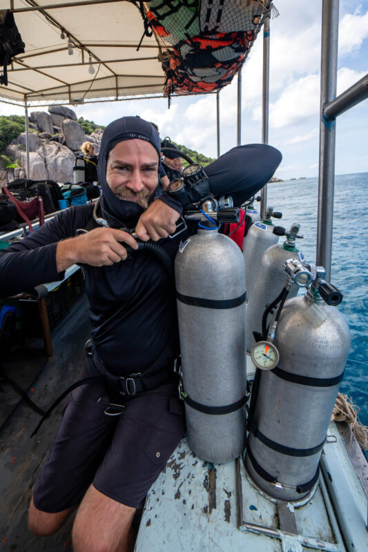 Scuba diver preparing equipment on boat with scenic ocean and rocky island background. Diving adventure setup.